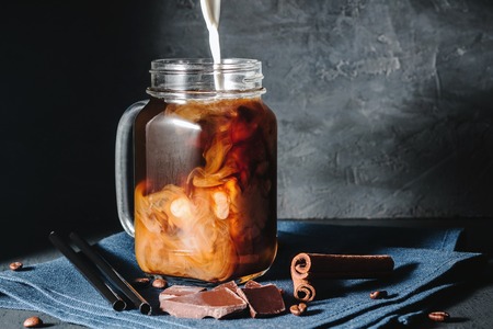 Coffee with ice and milk in a glass mason jars on the napkin at dark background.の写真素材