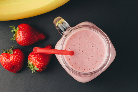 Smoothie with strawberry and banana in the jar at dark background, top view.