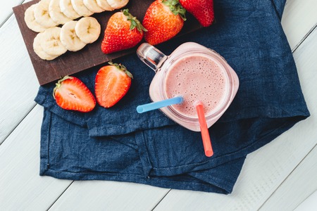 Smoothie with strawberry and banana in the jar at the white, wooden background with blue napkin, top view.の写真素材