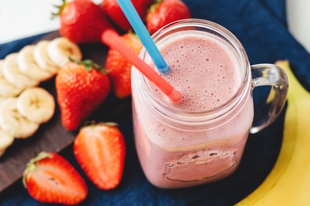 Smoothie with strawberry and banana in the jar at the white, wooden background with blue napkin.の写真素材