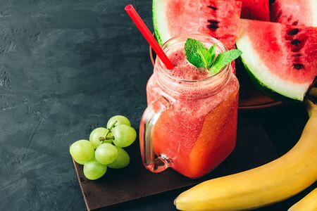 Watermelon red smoothie in jar with fresh mint leaves, banana and grape on dark background.の写真素材