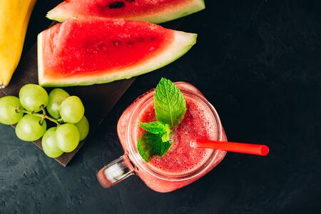 Watermelon red smoothie in jar with fresh mint leaves, banana and grape on dark background, top view.の写真素材