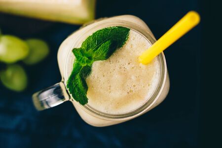 Melon smoothie in a jar with fresh mint leaves and grape on dark background, top view.の写真素材