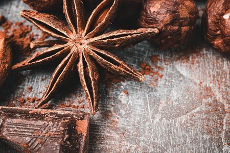 Star anise, chocolate cubes and nuts on grey textured background, close-up view.