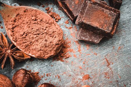 Brown cocoa powder in the spoon, chocolate cubes and nuts, top view.の写真素材