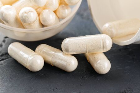 White medical capsules of glucosamine chondroitin, healthy supplement pills on dark background,...