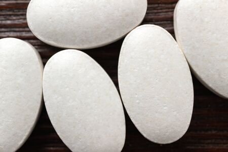 White medical supplement pills on wooden background, macro image, top view.
