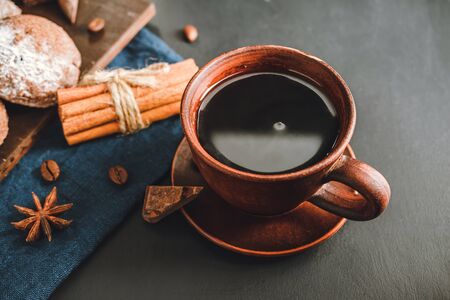 Brown cup with black coffee, cookies, cinnamon sticks, star anise on dark background.の写真素材