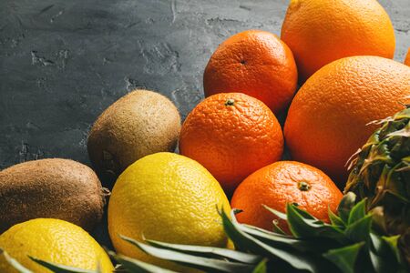 Assortment of tropical fruits, banana, kiwi, orange, tangerine, lemon, pineapple, grapefruit on dark background, copy-space.の写真素材