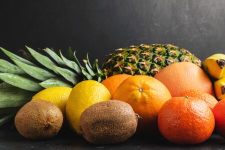 Assortment of tropical fruits, banana, kiwi, orange, tangerine, lemon, pineapple, grapefruit on dark background, copy-space.の写真素材