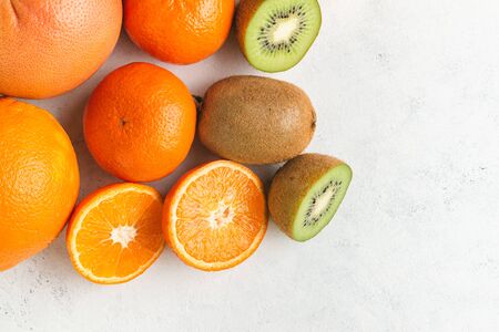 Assortment of tropical fruits, sliced and whole kiwi, orange, tangerine, grapefruit on textured white background, top view.の写真素材