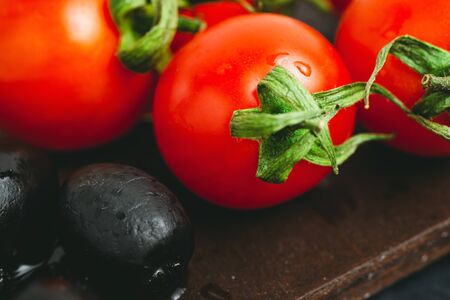 Red cherry tomato and black olives on wooden board.の写真素材