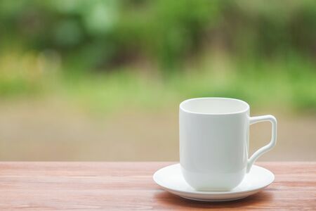 White porcelain cup on wooden table, blurred nature background.の写真素材