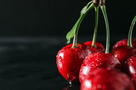 Fresh red cherries with water drops on dark background, close-up view.
