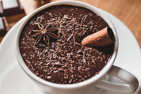 Hot chocolate drink in white cup with cinnamon stick and star anise on a wooden table, close-up...