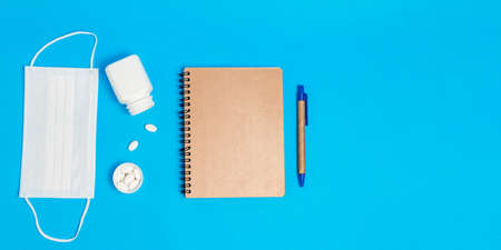 White medical mask, bottle with pills and notepad on blue background. Concepts of protection,...
