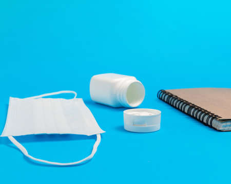White medical mask, bottle with pills and notepad on blue background. Concepts of protection, prevention and treatment coronavirus, covid 19, flu.の写真素材