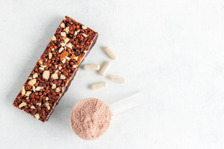 Scoop of whey or soy protein isolate, chocolate protein bar, white capsules of amino acids and creatine, bodybuilding food supplements on white background, top view, flat lay.の写真素材