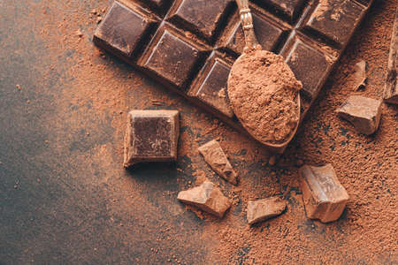 Brown cocoa powder in the spoon on chocolate bar and chopped chocolate cubes, top view on dark background with copy space.の写真素材