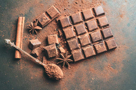 Brown cocoa powder in the spoon, chocolate bar and chopped chocolate cubes, top view on dark background with copy space.の写真素材