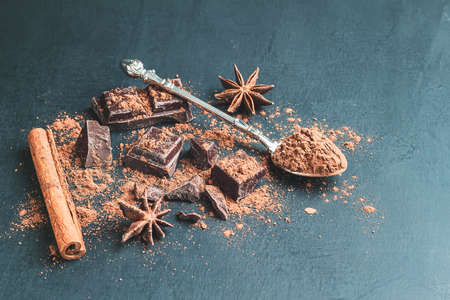 Brown cocoa powder in the spoon, chocolate cubes, cinnamon stick and star anise on dark background with copy space.の写真素材