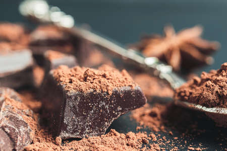 Chocolate chunk, chopped chocolate cubes with cocoa powder on dark background, close-up view.