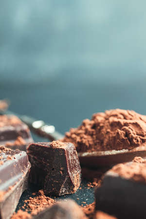 Chocolate chunk, chopped chocolate cubes with cocoa powder on dark background with copy space, close-up view.の写真素材
