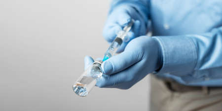 Male, doctor in blue shirt and gloves, holding in the hand a syringe and vaccine bottle against...