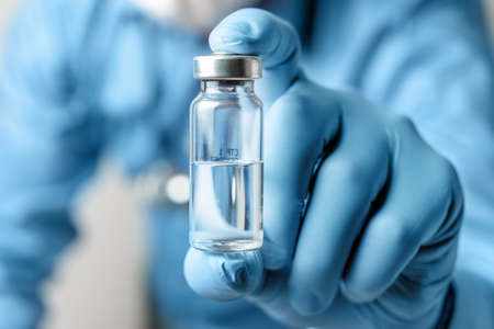 Male, doctor in blue shirt and gloves, holding in the hand vaccine bottle against disease or flu, vaccination concept.の写真素材