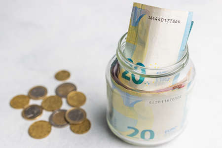 Euro banknotes in a glass jar and coins on a table, saving money concept with copy space.の写真素材