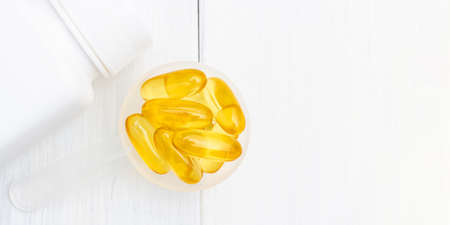 Omega-3 yellow capsules in a plastic scoop, nutritional supplements, close-up, top view.