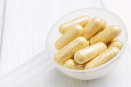Yellow herbal capsules in a plastic spoon, medication treatment, alternative medicine, close-up...