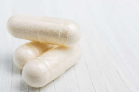 White pills or capsules at white wooden planks, medication treatment, alternative medicine, close-up view.の写真素材