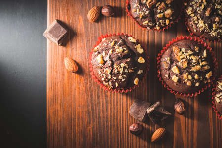 Homemade chocolate muffins or cupcakes sprinkled of nuts on a wooden board, top view.の写真素材