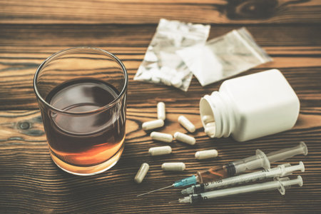 Glass with alcohol drink, whiskey or brandy, white pills, syringe with a drug dose, narcotic in...