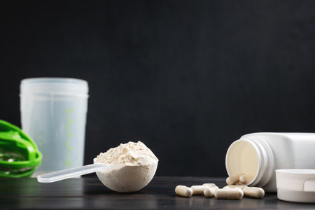 Scoop of whey or soy protein powder, white capsules of amino acids, vitamins and creatine,...