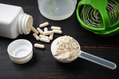 Scoop of whey or soy protein powder, white capsules of amino acids, vitamins and creatine, bodybuilding food supplements, sports nutrition, plastic shaker on a dark wooden board.の写真素材