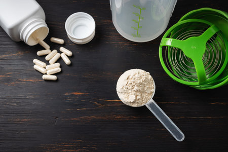 Scoop of whey or soy protein, white capsules of amino acids, vitamins and creatine, bodybuilding food supplements, sports nutrition, shaker on a dark wooden board, top view.の写真素材