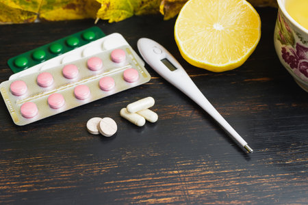 Capsules, pills, medicine in a blister pack, thermometer, lemon on a wooden table with yellow...
