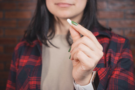 Young woman takes a medicine, holds white pill in a hand, close-up view.