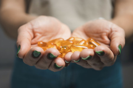 Young woman holds pile of omega-3 fish oil supplements, vitamin yellow capsules in her hands,...