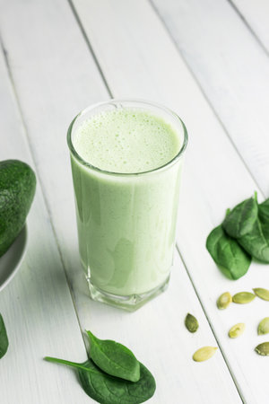 Green detox smoothie, blended vegetarian drink in a glass from spinach, apple, avocado and seeds on white wooden table, healthy eating concept.の写真素材