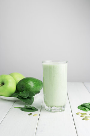 Green detox smoothie, blended vegetarian drink in a glass from spinach, apple, avocado and seeds on white wooden table, healthy eating concept.の写真素材