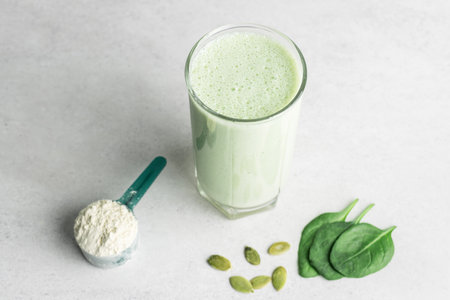 Green detox smoothie, blended vegetarian drink in a glass from protein powder, spinach and seeds on a table, healthy eating concept.の写真素材