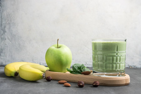 Green detox smoothie in a glass, blended vegetarian drink from spinach leaves, apple, banana fruit and nuts, healthy eating concept.の写真素材