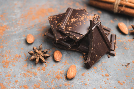Heap of delicious dark chocolate pieces or cubes, chopped, broken chocolate bar, almond nut, cinnamon sticks and star anise on a dark background.の写真素材
