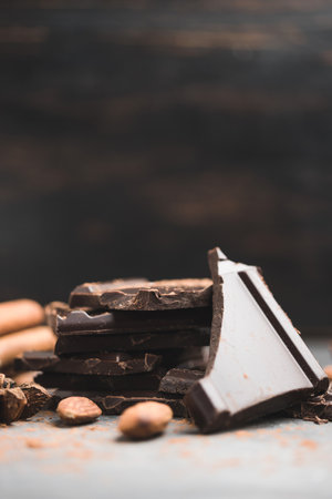 Heap of delicious dark chocolate pieces or cubes, chopped, broken chocolate bar, almond nut, cinnamon sticks and star anise on a dark background.の写真素材