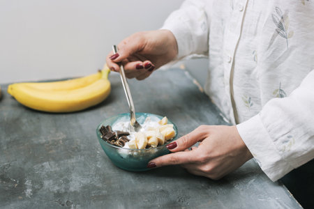 Woman eating healthy food for breakfast, cereal, granola, muesli, oatmeal with banana, dark chocolate and yogurt in a bowl.の写真素材