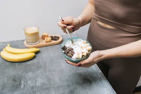 Athletic woman in sportswear eating healthy food for breakfast, cereal, granola, muesli, oatmeal with banana, dark chocolate and yogurt in a bowl.の写真素材