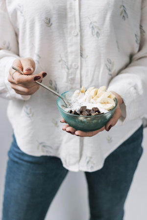 Woman eating healthy food for breakfast, cereal, granola, muesli, oatmeal with banana, dark chocolate and yogurt in a bowl.の写真素材